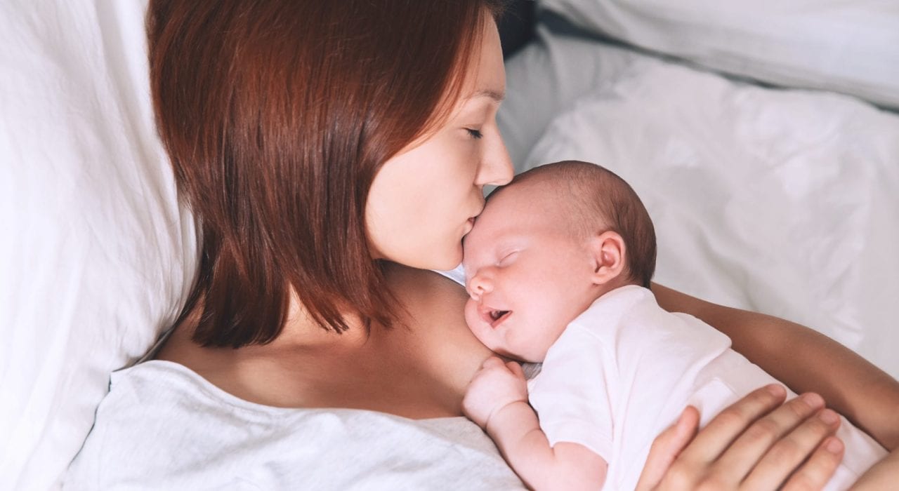 newborn - New mother hugging and kissing her newborn baby on hte forehead