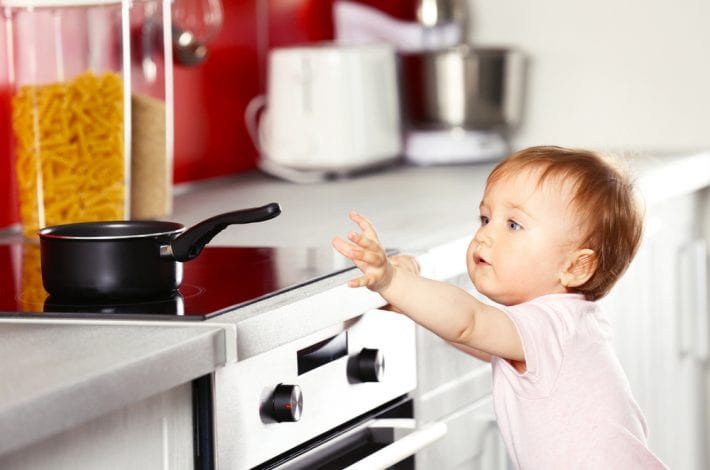 child reaching for hot pot on stove - babyproofing home