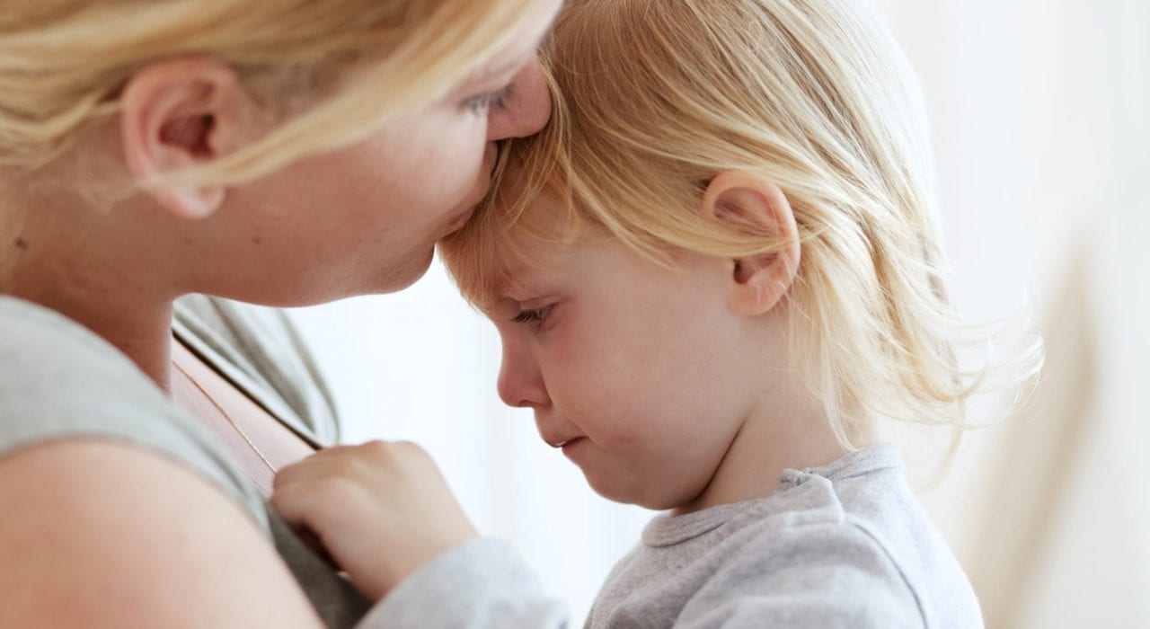 mother kissing crying toddler on forehead - managing terrible twos